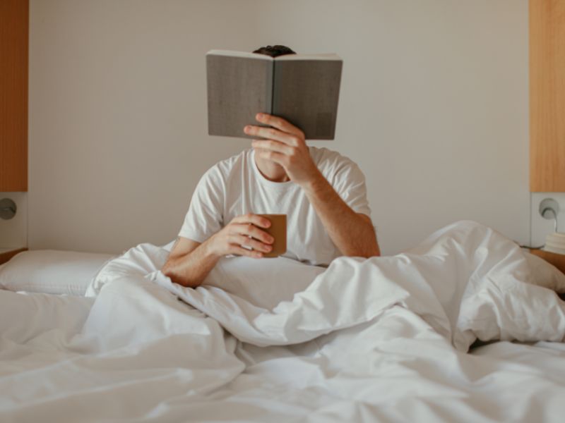 Person reading a book in bed in Canberra accommodation.