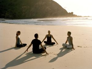 people sitting on a beaching doing yoga.