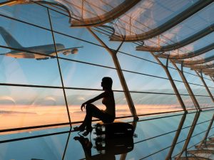 Female sitting by a window at the airport watching the planes take off and land.