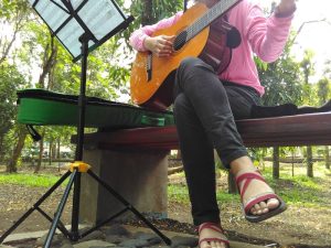 female busker playing guitar in a park.